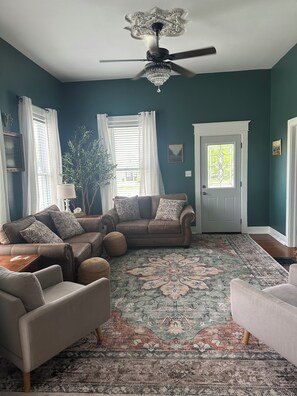 A living room with a ceiling fan, a patterned rug, a brown leather sofa, and a door with a stained glass window. - Verbena Executive Cottage (Morris)