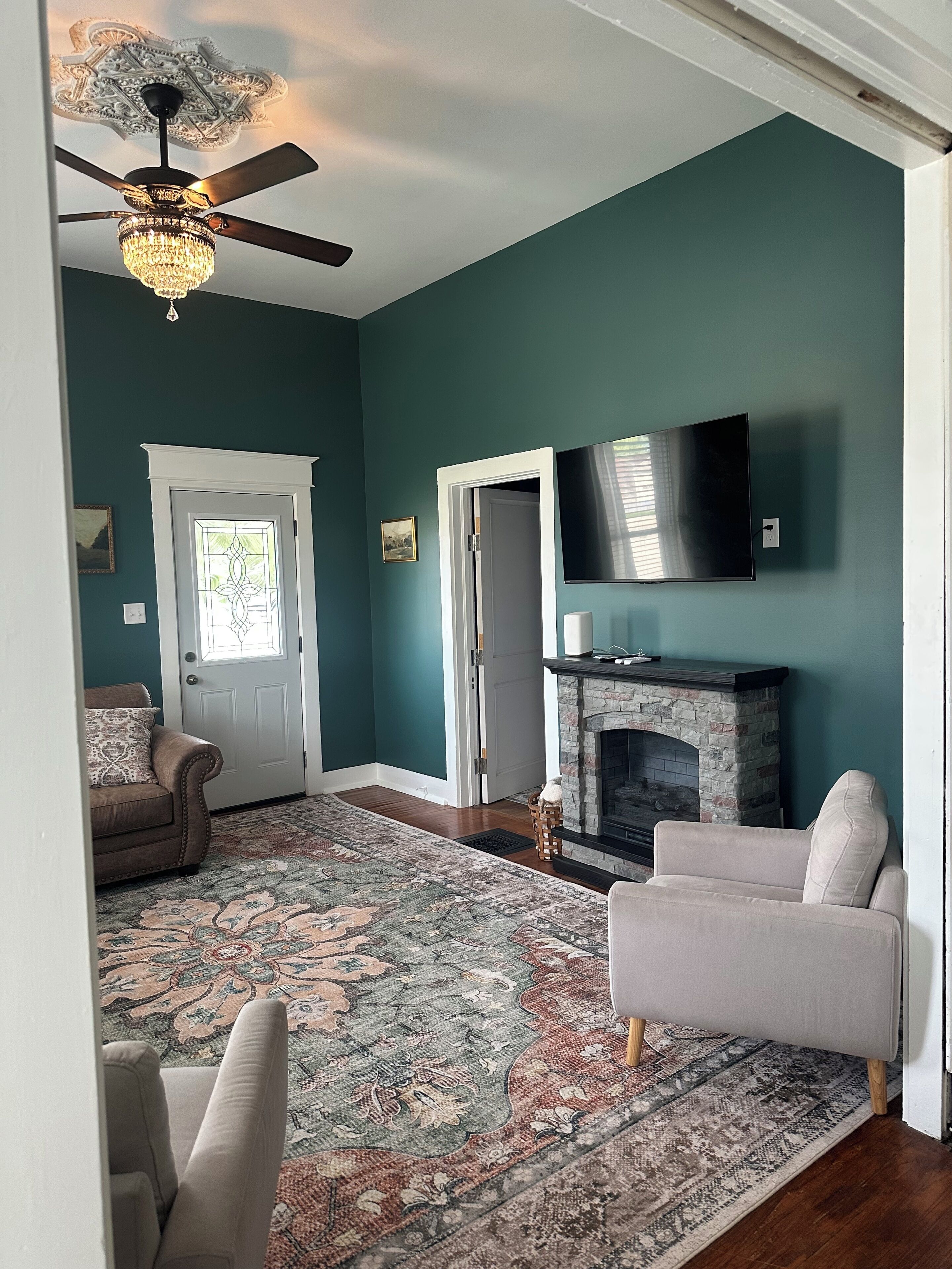 A living room with a fireplace, a television, a ceiling fan, and a patterned rug.. Verbena Executive Cottage
