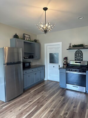 A kitchen with a stainless steel refrigerator, gray cabinets, a white door, and a black stove. - Verbena Executive Cottage (Morris)