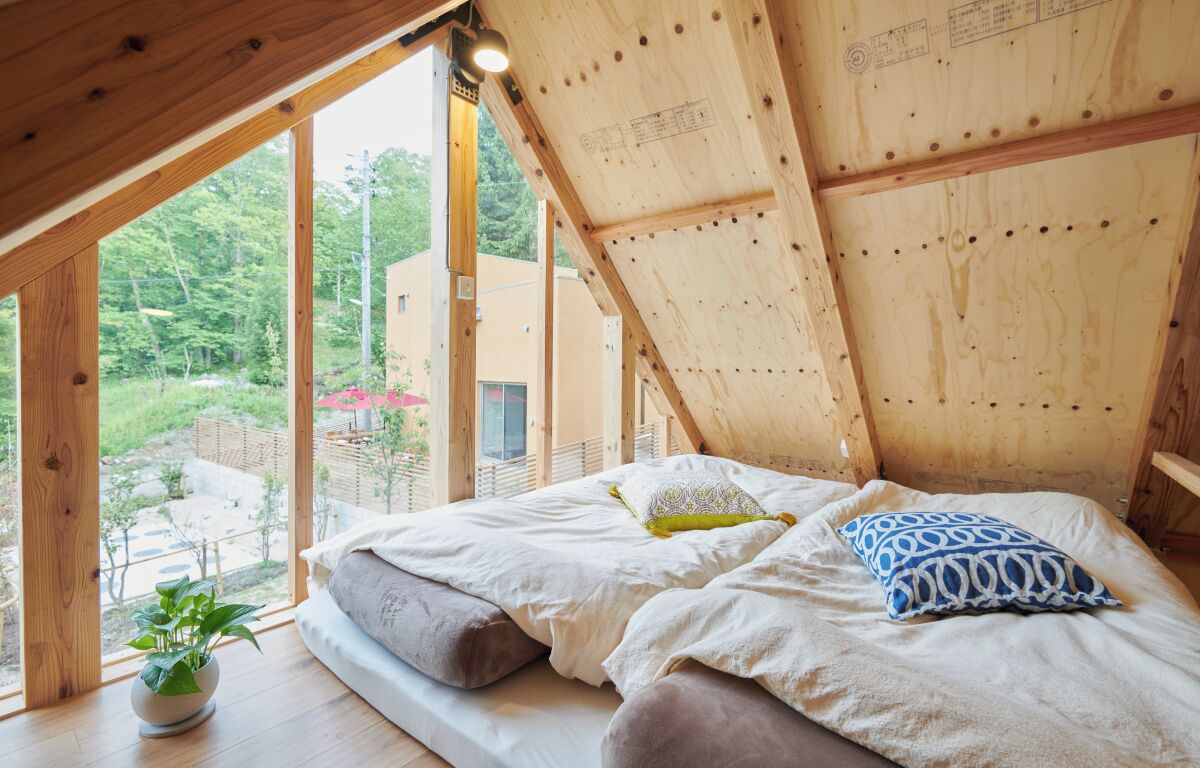 Um quarto com teto de madeira, uma cama com almofadas e um vaso de planta.