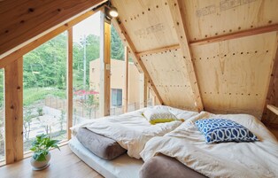 A bedroom with a wooden ceiling, a bed with pillows, and a potted plant.