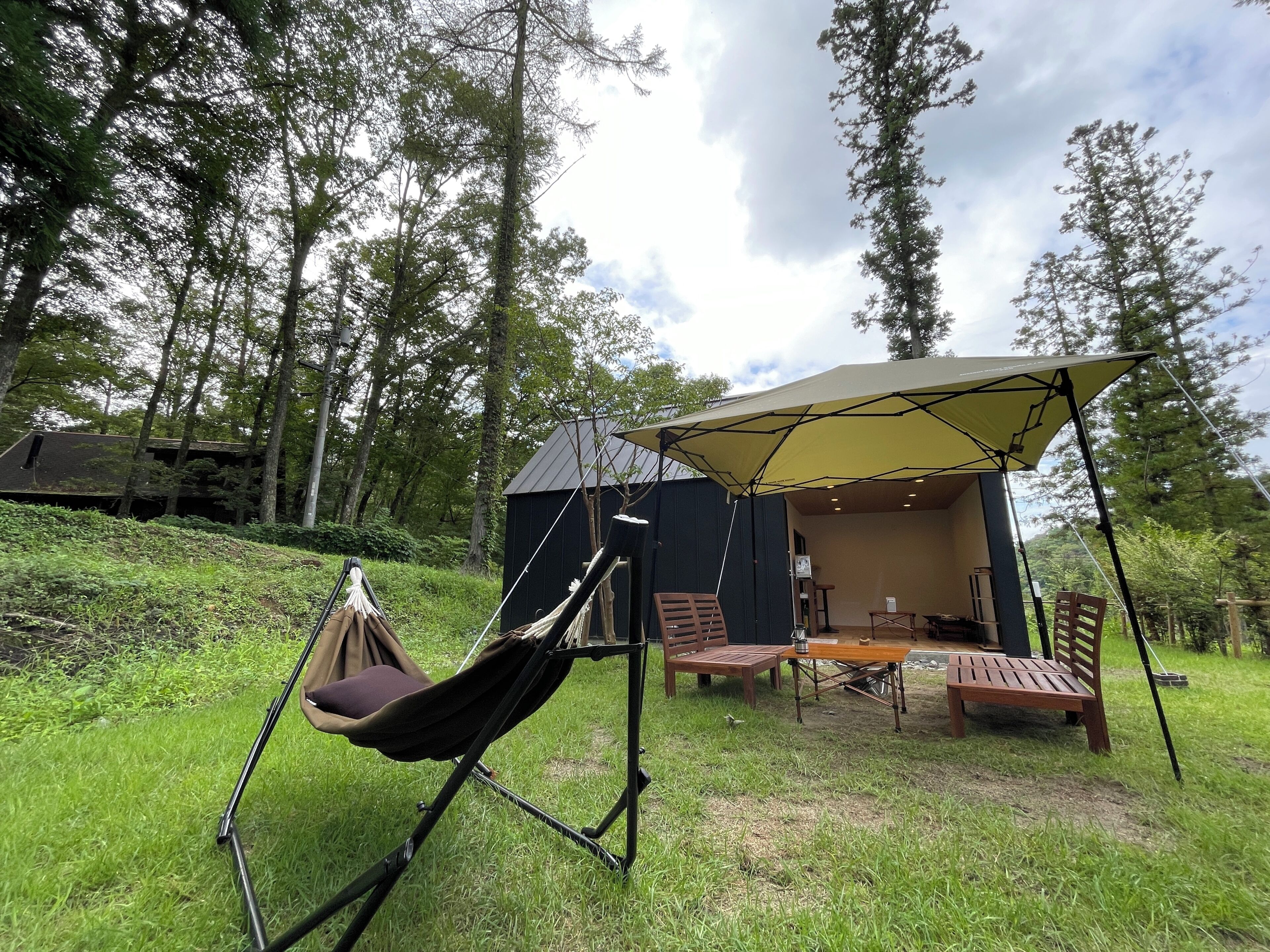 A tented outdoor area with a hammock, wooden table, chairs, and a small building.