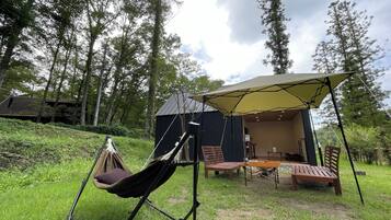 A tented outdoor area with a hammock, wooden table, chairs, and a small building.