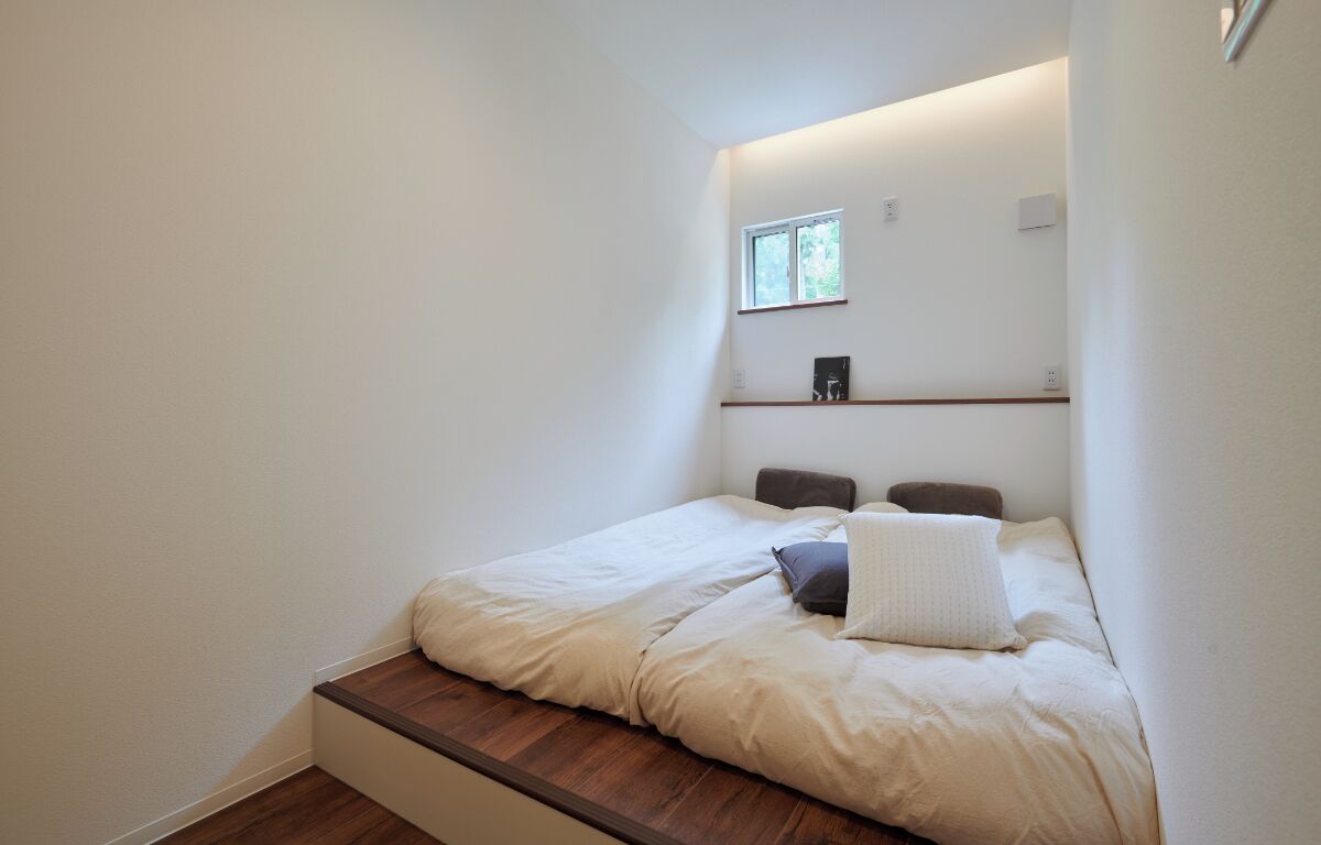 Quarto pequeno e moderno, com uma cama de solteiro, uma janela e uma prateleira com alguns objetos.