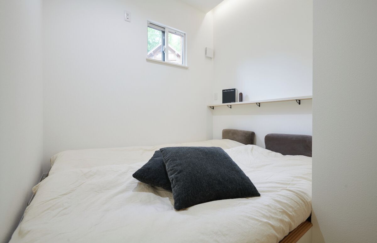 Quarto com cama, travesseiros, janela e uma prateleira com um livro.