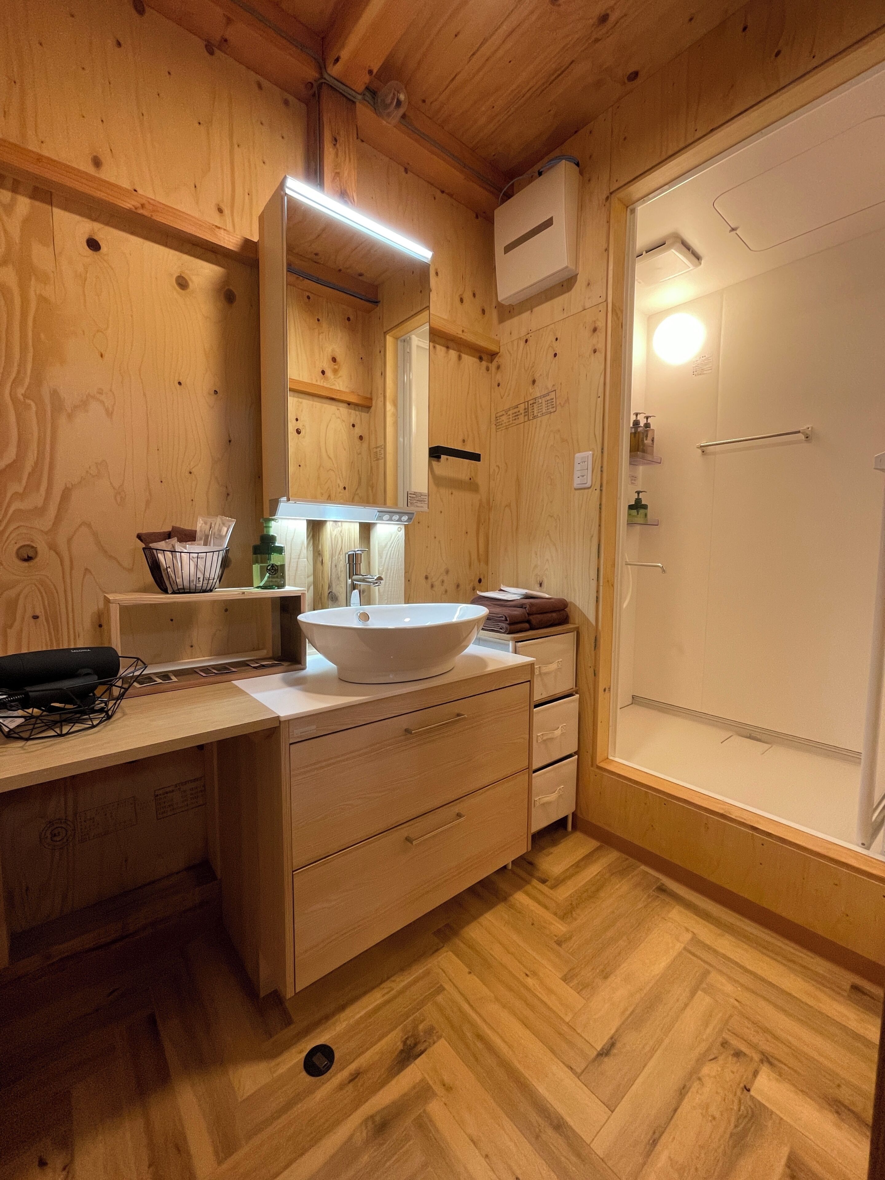 A wooden cabin-style bathroom with a wooden vanity, a white sink, a mirror, and a shower area.