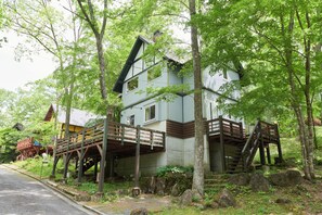 A two-story house with a wooden deck and stairs, surrounded by trees. - morinoretreat  foresta di luce (Hatsukaichi)