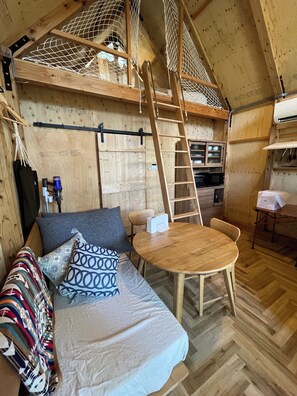 Een gezellig chaletinterieur met een vide, een houten eettafel, een keukenhoek en een bank met opvallende kussens.