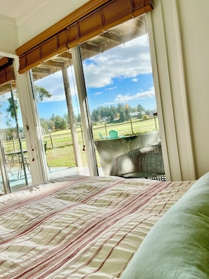 Une chambre avec un grand lit, donnant sur un champ verdoyant, et une terrasse avec une chaise.
