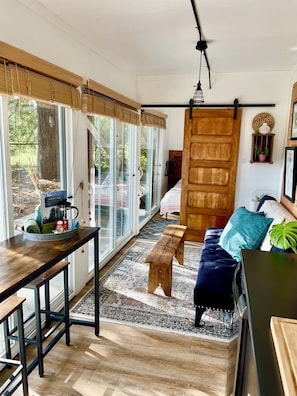 Un intĂ©rieur moderne avec un banc en bois, un canapĂ©, une table Ă manger et une grande porte-fenĂȘtre coulissante donnant sur un espace extĂ©rieur.