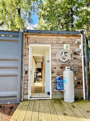 Une petite cabane en bois avec une porte donnant sur un intérieur comprenant un lit et une table.