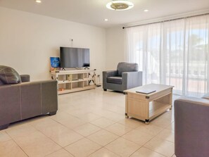 Ein modernes Wohnzimmer mit Flachbildfernseher, einer Couch, einem Sessel und einem Holztisch.