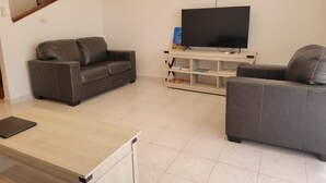 Un soggiorno con due divani grigi, una televisione a schermo piatto, un tavolino in legno e una libreria.