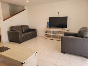 A living room with two grey sofas, a flat-screen TV, a wooden coffee table, and a bookshelf. - The Harbour Nest 2BR Sleeps 4 (Saint John's)