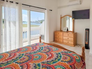 Ein Schlafzimmer mit Bett, Kommode, Spiegel, Fernseher und Blick auf eine Marina.