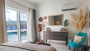 Une chambre avec un grand lit, une commode, une chaise et une vue sur la mer.