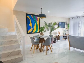 A modern living room with a dining area, a staircase, and a large abstract painting on the wall. - Lazy Gecko Stylish with spacious deck (Saint John's)