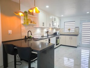 A modern kitchen with a central island, white cabinets, and pendant lighting. - Lazy Gecko Stylish with spacious deck (Saint John's)