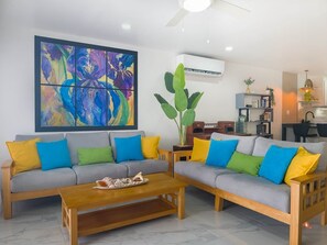 A living room with two sofas, a coffee table, and a large abstract painting. - Lazy Gecko Stylish with spacious deck (Saint John's)