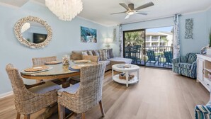 A spacious living area with a dining table, wicker chairs, a sofa, a round coffee table, and a ceiling fan. - The Turtle Nest Coastal Escape (St. Augustine)