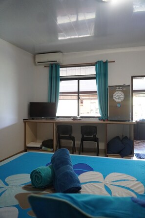 A hotel room with a bed, a desk with a computer, a water cooler, and a window with curtains.