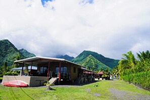 Ein Gebäude mit überdachter Außenfläche, Stufen, die davor führen, und Blick auf grüne Berge im Hintergrund.