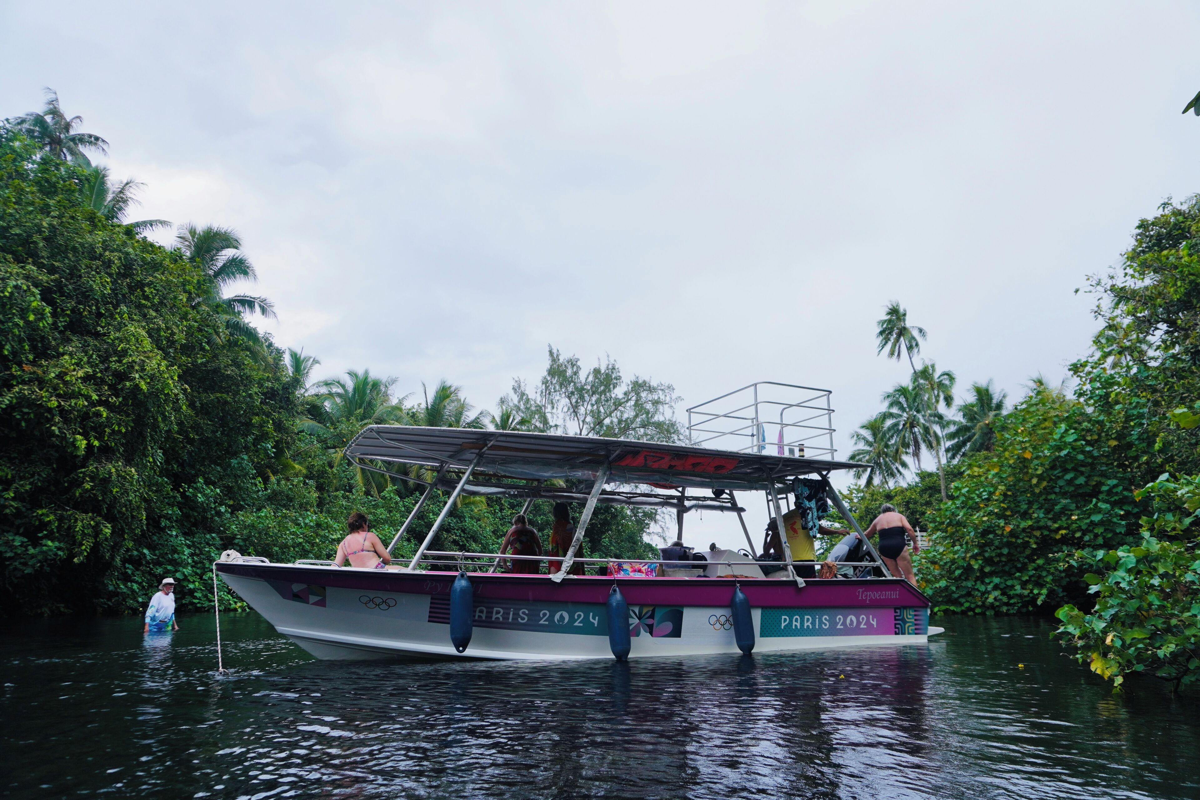 A boat with 'PARIS 2024' written on it, surrounded by lush greenery.