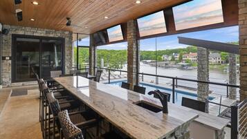 Un vaste espace extérieur aménagé pour les repas, avec une longue table et des chaises, offrant une vue sur une rivière et sur des bâtiments.