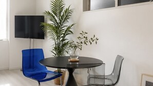 Ein moderner Essbereich mit einem runden Tisch, zwei Stühlen, einer Topfpflanze und einem Flachbildfernseher an der Wand.