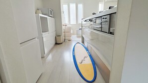 Eine schmale Küche mit weißen Schränken, einer Mikrowelle und einem Surfbrett auf dem Boden.