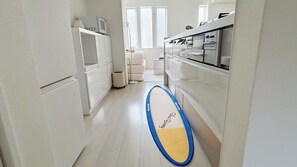 Een smalle keuken met witte kastjes, een magnetron en een surfplank op de vloer.