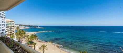 A coastal view with a beach, ocean, and a building with balconies overlooking the sea.