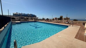 A swimming pool with a clear view of the sea, lounge chairs, and a building with solar panels. - Marbell Center Panoramic Sea View (Marbella)