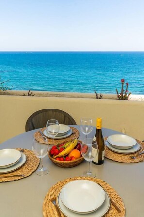 Una mesa para dos personas, con platos, copas, una botella de vino y una cesta de fruta.