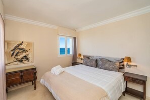 A bedroom with a bed, a nightstand, a lamp, a painting, and a window with a view. - Marbell Center Panoramic Sea View (Marbella)