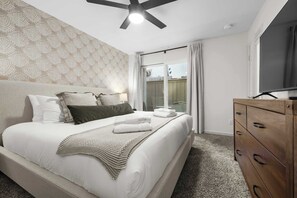 Ein Schlafzimmer mit einem Bett, einem Deckenventilator, einer Kommode und einem großen Fenster.