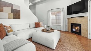 A modern living room with a sectional sofa, a flat-screen TV, a fireplace, and a large abstract painting on the wall. - Pacific Beach Townhouse | BBQ | Rooftop | Vibes (San Diego)