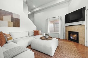 Ein modernes Wohnzimmer mit Ecksofa, Flachbildfernseher, Kamin und einem großen abstrakten Gemälde an der Wand.