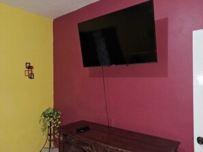 Quarto com televisão fixada numa parede vermelha, cómoda de madeira e parede amarela.