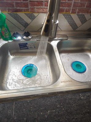 Uma pia de cozinha com duas tampas azuis de escoamento e uma garrafa de detergente.