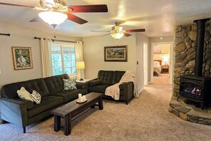 A living room with a sofa, a coffee table, a fireplace, and ceiling fans. - Family Friendly Cottage w/ Meadowview, Hot Tub, Large Deck, WiFi & Private W/D (Avery)