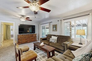 A living room with a ceiling fan, a television, a sofa, a coffee table, and a window with curtains. - Family Friendly Cabin w/ Meadow View, Hot Tub, Large Deck, WiFi & Private W/D (Avery)