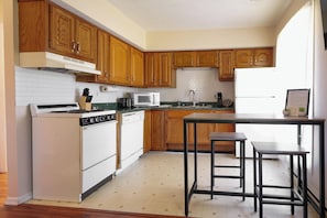 A kitchen with wooden cabinets, a stove, a microwave, a dishwasher, and a table with stools.