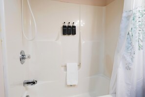 A bathroom with a bathtub, a shower, and a toilet. There are three bottles of shampoo and conditioner on the wall.