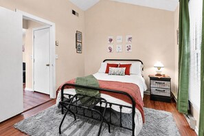 Ein Schlafzimmer mit einem Bett, einem Nachttisch, einer Lampe und Kunstwerken an der Wand.