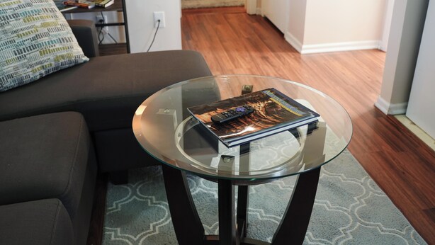 Uma sala de estar com uma mesa de centro de vidro, um sofá e uma estante.
