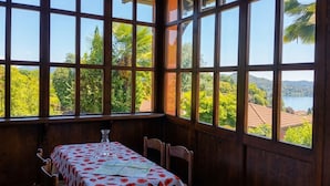 Een kamer met een gedekte tafel voor twee, grote ramen met uitzicht op groen en een waterpartij.