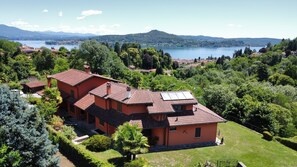 A large house with multiple sections, surrounded by lush greenery and a lake.