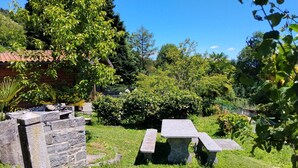 Een stenen bank en tafel in een tuin, met een huis op de achtergrond.