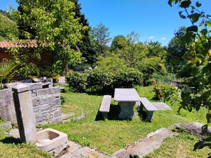 Eine Steinsitzbank und ein Steintisch in einem Garten mit einem Haus im Hintergrund.